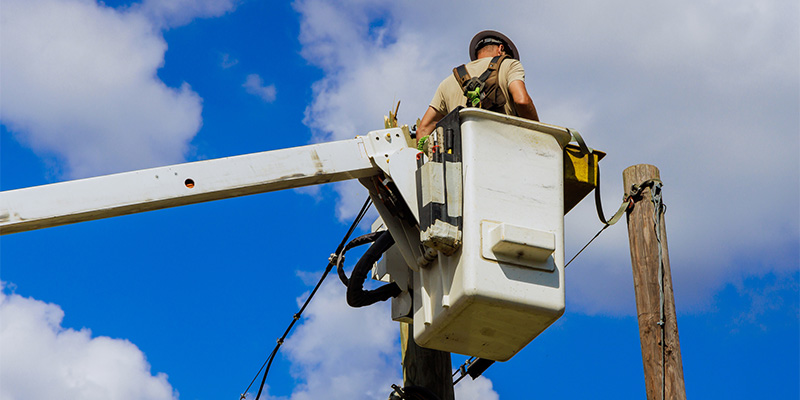 Utility worker repairs electrical lines on clear day in residential area surrounded by blue skies